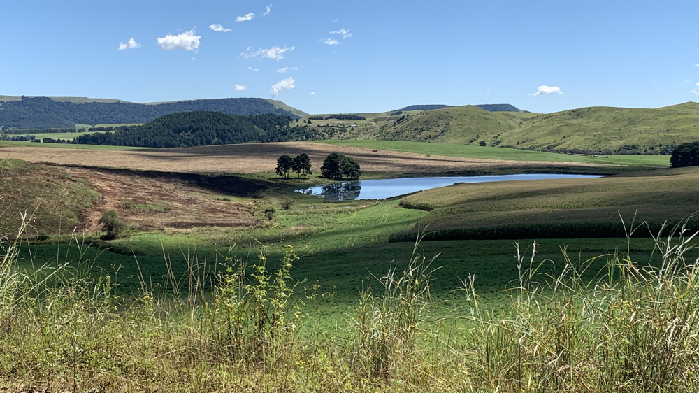A dam with fields in. the foreground and hills behind.