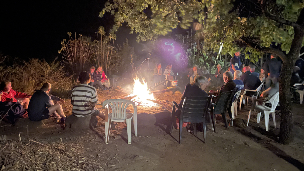 A large group sitting around a big fire in the evening.