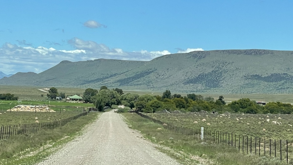 Gravel road with a farm, green fields and hills.